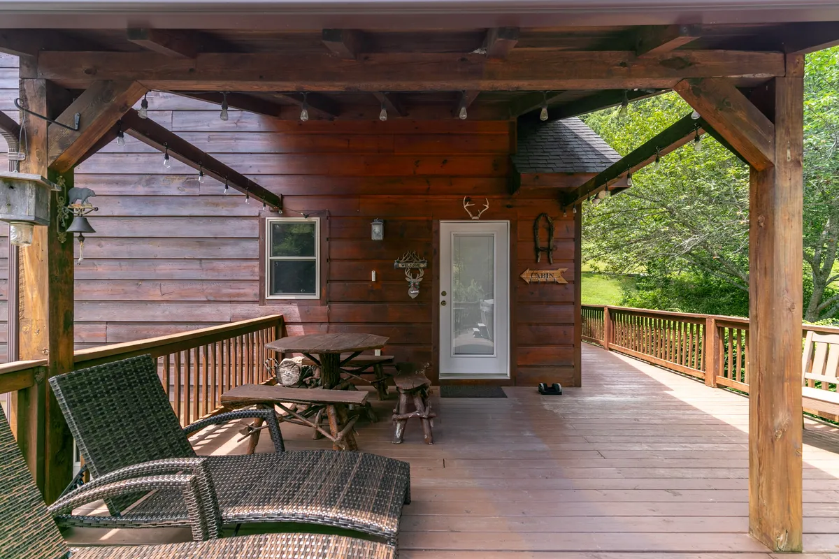 A cozy wooden deck with hanging lights, comfortable outdoor furniture, and adjoining wall—set up for socializing, dining, or simply relaxing. The setting is inviting, enveloped by nature, and suggests a space that is both private and open to the outdoors.