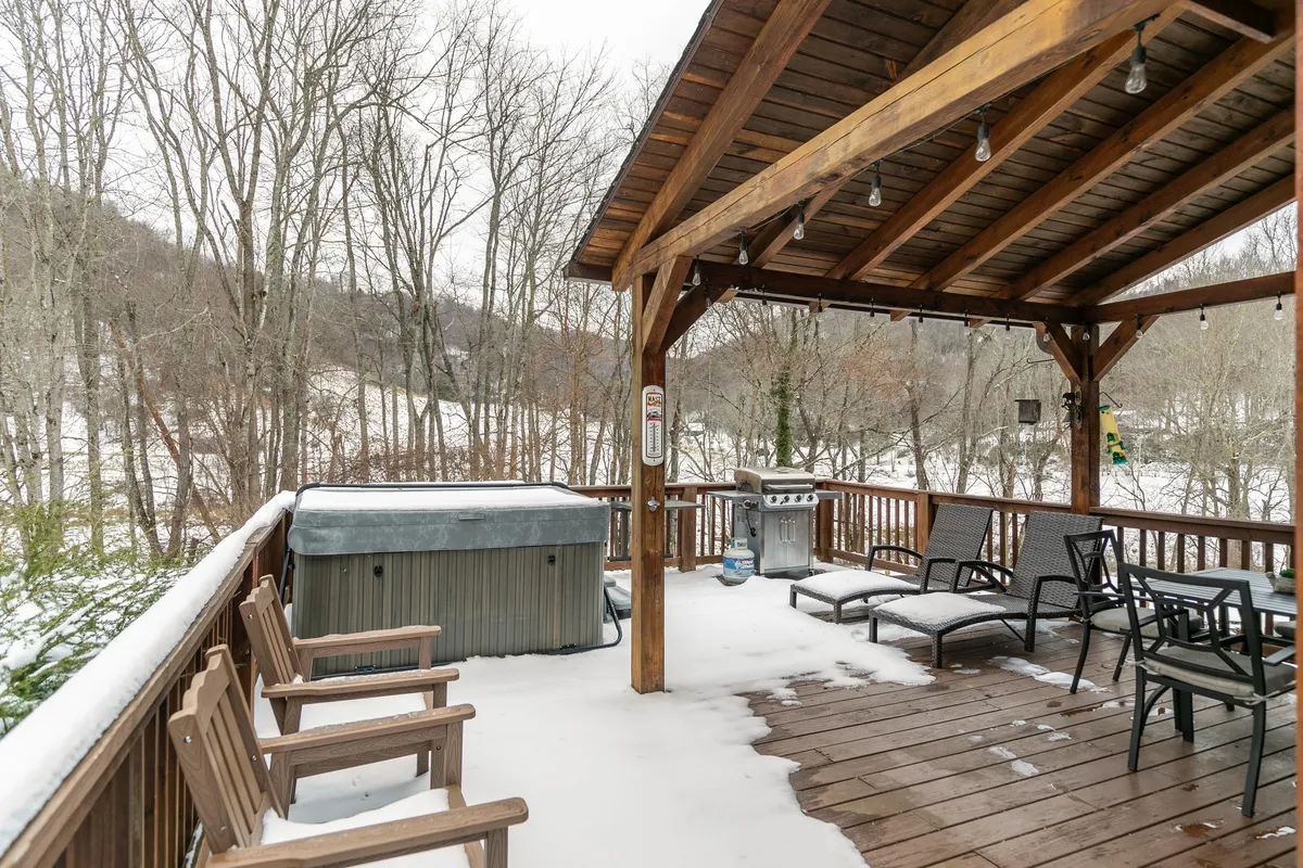 This photo shows a wooden deck with a bubbling hot tub, outdoor seating, and a grill, all surrounded by tranquil mountain views. The space is set up for both relaxation and stargazing with friends or loved ones.