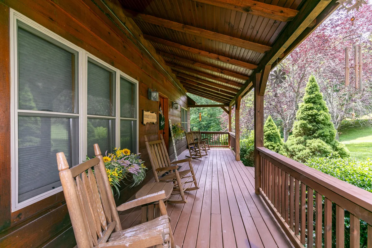 This image features a classic wooden porch with rocking chairs, colorful flower pots, and lush greenery surrounding the cabin, evoking a peaceful retreat into nature. The inviting porch is ideal for relaxing, sharing stories, and enjoying mountain views with family after a day outdoors.