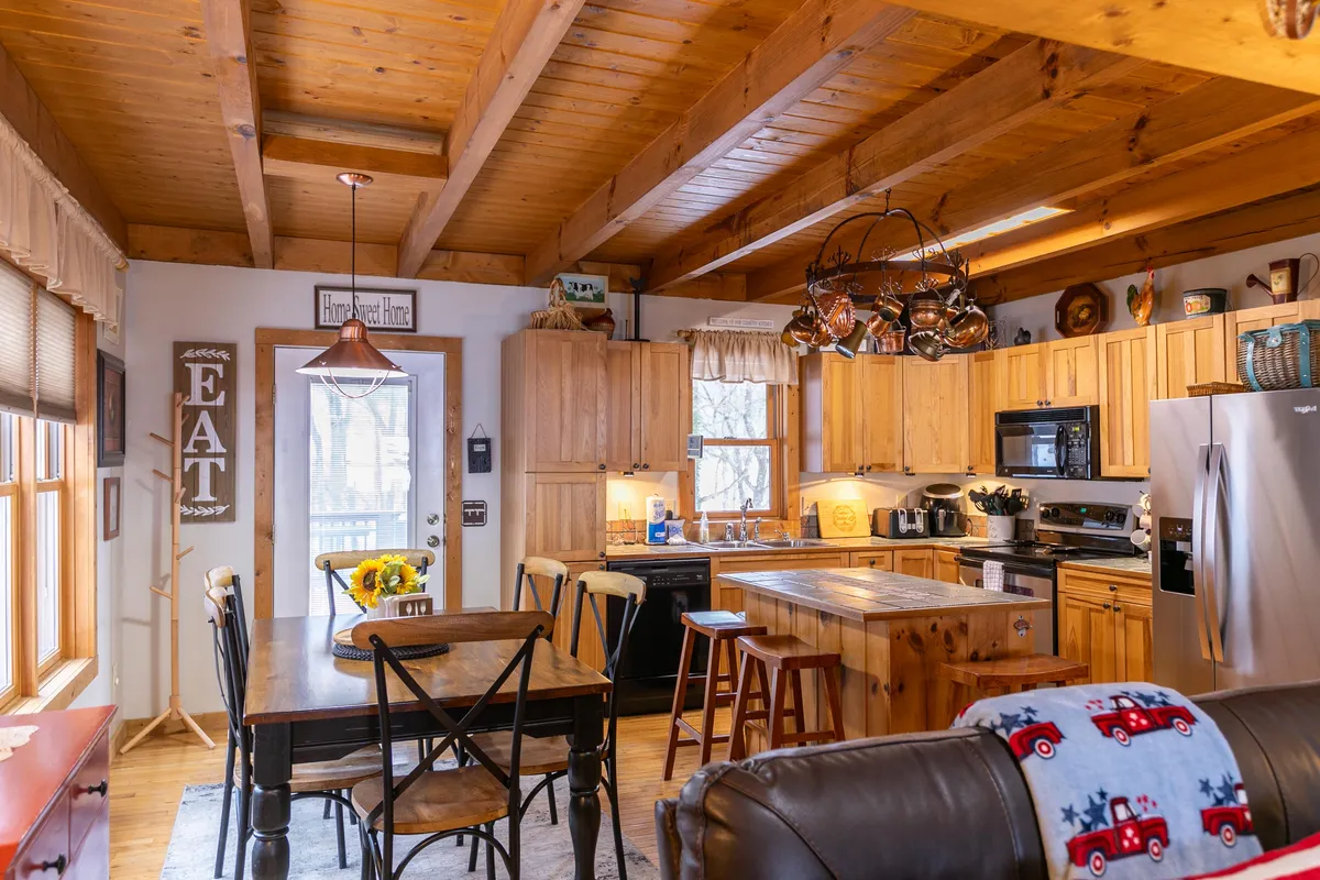 A bright dining area with a wooden table, kitchen island, exposed wooden beams, and decorative elements. The space feels welcoming and is designed for cooking, entertaining, and memorable family meals.