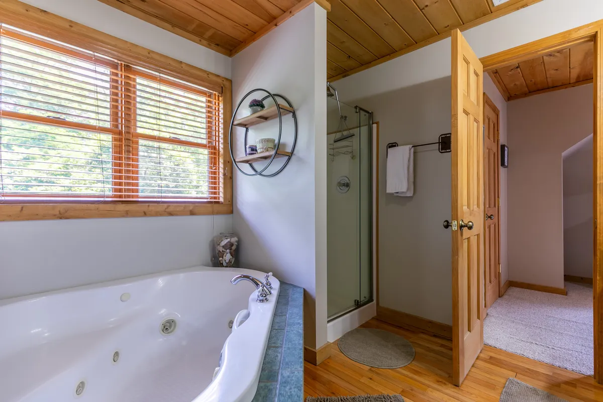 A modern bathroom featuring a jacuzzi tub, glass shower, and wooden ceiling—creating a spa-like retreat. The layout and finishes suggest an upgraded, indulgent experience, ideal for unwinding after a long day.