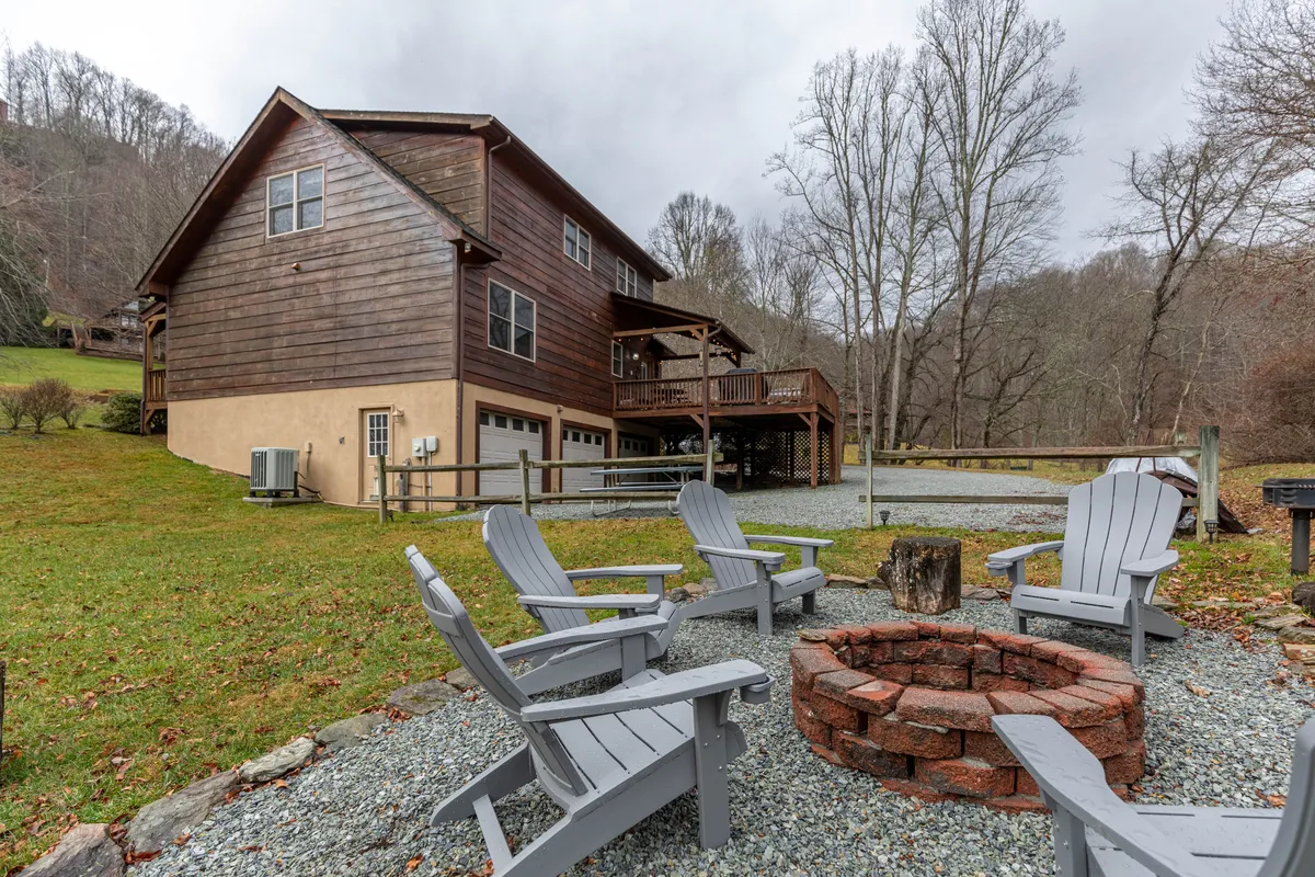 A cozy outdoor space featuring a fire pit surrounded by Adirondack chairs, a wooden deck, and expansive natural landscaping—ideal for gatherings, relaxation, and enjoying the outdoors with neighbors or family.