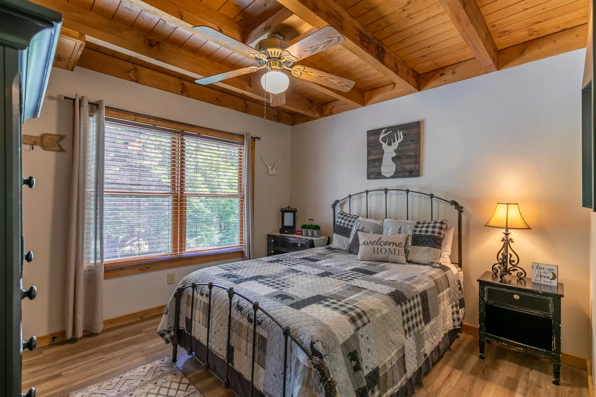 A warmly lit bedroom featuring a cozy bed with patterned bedding, a window allowing natural light to pour in, and charming decorative wall art. The LVP flooring and neutral palette create a relaxing and inviting atmosphere, perfectly suited for a restful night’s sleep.
