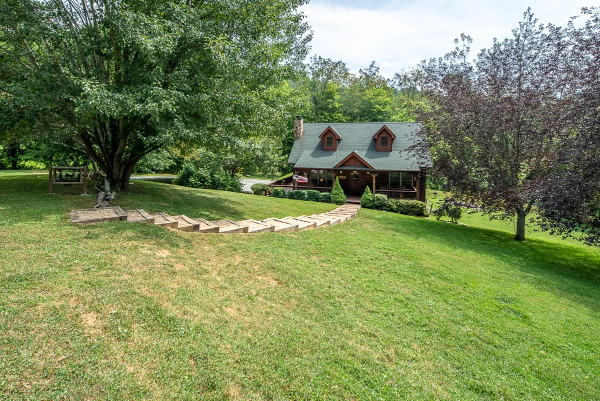 A wide shot of the cabin’s exterior is shown, with the house nestled among trees, a welcoming pathway, and ample open lawn space perfect for kids and pets to play. The image captures the spirit of family-friendly outdoor adventures and the spaciousness described in the text.
