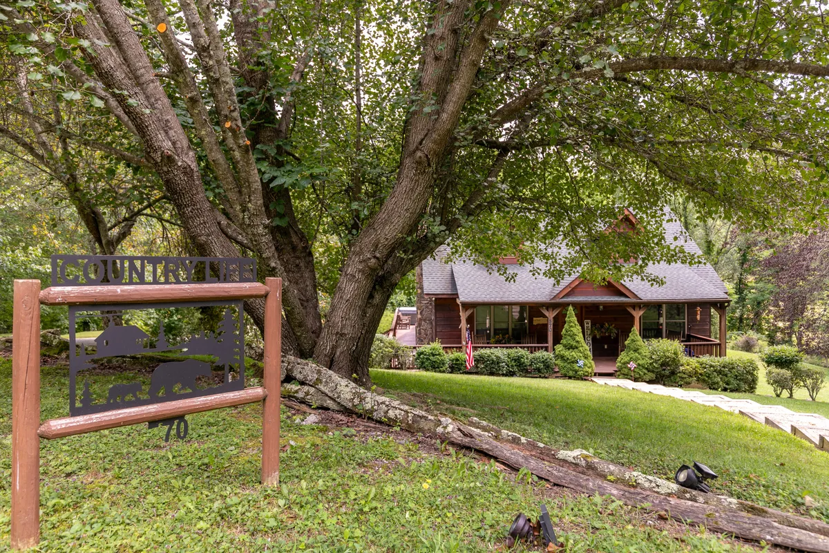 A rustic wooden sign engraved with 'COUNTRY' sits beside a charming wooden house, enveloped by lush greenery, hinting at the inviting, close-knit atmosphere of the development.